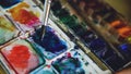 Young woman artist draw pictrure with watercolor paints. Closeup brush mixing colors in pallete Royalty Free Stock Photo