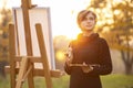 Young woman artist drawing a picture on an easel in nature at sunset in autumn,concept of creativity and a hobby