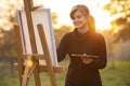 Young woman artist drawing a picture on an easel in nature at sunset in autumn,concept of creativity and a hobby