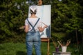 A young woman artist holds a brush and paints a picture on an easel in the rays of the sunset. The painter paints oil paintings in Royalty Free Stock Photo