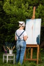 A young woman artist holds a brush and paints a picture on an easel in the rays of the sunset. The painter paints oil paintings in Royalty Free Stock Photo