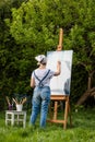 A young woman artist holds a brush and paints a picture on an easel in the rays of the sunset. The painter paints oil paintings in Royalty Free Stock Photo