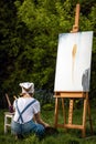 A young woman artist holds a brush and paints a picture on an easel in the rays of the sunset. The painter paints oil paintings in Royalty Free Stock Photo