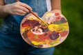 A young woman artist holds a brush and paints a picture on an easel in the rays of the sunset. The painter paints oil paintings in Royalty Free Stock Photo