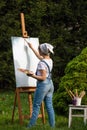 A young woman artist holds a brush and paints a picture on an easel in the rays of the sunset. The painter paints oil paintings in Royalty Free Stock Photo