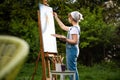 A young woman artist holds a brush and paints a picture on an easel in the rays of the sunset. The painter paints oil paintings in Royalty Free Stock Photo