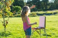 A young woman artist holds a brush and paints a picture on an easel of the sunset