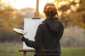 Young woman artist in nature drawing a picture on canvas on an easel in nature