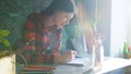 Young woman artist painting sketch on paper notebook with pencil. Bright sun flare from window Royalty Free Stock Photo