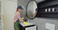 Young woman as a professional cleaner in uniform cleaning bathroom. Cleaning service concept. Royalty Free Stock Photo