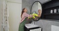 Young woman as a professional cleaner in uniform cleaning bathroom. Cleaning service concept. Royalty Free Stock Photo