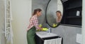 Young woman as a professional cleaner in uniform cleaning bathroom. Cleaning service concept. Royalty Free Stock Photo