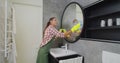 Young woman as a professional cleaner in uniform cleaning bathroom. Cleaning service concept. Royalty Free Stock Photo