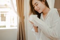 Young woman asia living at home relaxing and drinking cup of hot coffee in the bedroom on holiday. Royalty Free Stock Photo