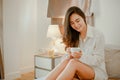 Young woman asia living at home relaxing and drinking cup of hot coffee in the bedroom on holiday. Royalty Free Stock Photo