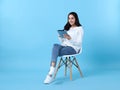Young woman asian happy smiling in casual white cardigan with denim jeans.While her using tablet computer sitting on white chair Royalty Free Stock Photo