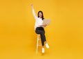 Young woman asian happy smiling celebrate. While her using laptop sitting on white chair isolate on bright yellow background Royalty Free Stock Photo
