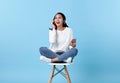 Young woman asian happy smiling wearing wireless headphones listening to music from smartphone on white chair isolate on bright Royalty Free Stock Photo