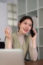 Young woman asian talking on mobile phone while working with laptop at desk home Royalty Free Stock Photo