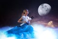 Young woman astronomer, dreamer. Girl sitting on the clouds with a telescope in hands. The moon in the starry sky