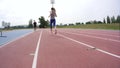 A young woman athlete in red snikers running past the camera during a day running training at the city athletics stadium