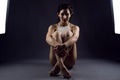 Young woman athlete in white top sitting on the floor between two studio flash lights embracing her crossed legs