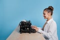 young woman author at a typewriter, writes a text. A writer at a table with a vintage typewriter