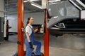 Young woman auto technician turning on car lift mechanism