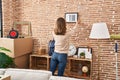 Young woman on back view hanging picture on wall at new home