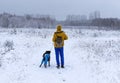 Young woman from the back in yellow winter clothes walking with a fluffy gray dog in a winter snowy forest Royalty Free Stock Photo