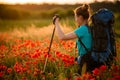 Young woman with backpack and walking sticks stands on field of poppies Royalty Free Stock Photo