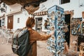 Young woman with backpack is looking at a postcard stand in a small spain village