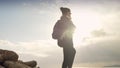 Young woman with a backpack, standing on the edge of a cliff, mesmerized by the breathtaking winter sunset over the sea.