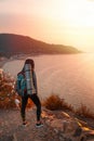 A young woman with a backpack, standing on the edge of a cliff. Rear view. In the background, the sea, the mountain and the sky at Royalty Free Stock Photo