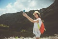 Young woman with backpack taking selfie photo with mobile phone. High mountains touristic path