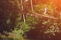 Young woman with backpack walking across hanging bridge above the river in forest Royalty Free Stock Photo