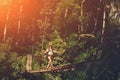 Young woman with backpack walking across hanging bridge above the river in green forest Royalty Free Stock Photo