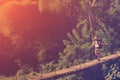 Young woman with backpack walking across hanging bridge in green forest Royalty Free Stock Photo