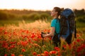 Young woman with backpack and walking sticks stands on field of poppies and looks away Royalty Free Stock Photo