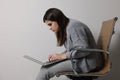 Young woman with bad posture using laptop while sitting on chair against background Royalty Free Stock Photo