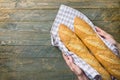 Young woman baker holds in hands freshly baked French baguettes in cotton towel on rustic wood kitchen table. Baking local food Royalty Free Stock Photo