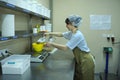 Young woman baker putting flour with measuring spoon in a pan placed on a weigher, bakery