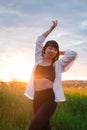 young woman in baldric on the summer field on sunset or sunrise. peaceful calm female. trendy clothes