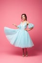 A young woman in a ball gown stands at a pink background. A beautiful brunette in a lush blue dress with lantern sleeves Royalty Free Stock Photo