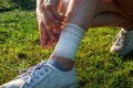 Young woman bandaging injured ankle. Injury leg while running outdoors. First aid for sprained ligament or tendon