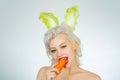 Young woman with banny ears eat carrot. Cute bunny rabbit. Easter bunny dress.