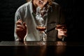 Young woman bartender holds tweezers with smoking stick near glass