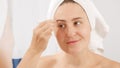 Young woman in bath towel using tweezers for plucking eyebrows. Concept of beautiful female, makeup at home, skin care and Royalty Free Stock Photo