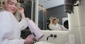 Young woman in bathrobe drying hair with a hairdryer in the bathroom at home. Usual morning beauty treatments in the Royalty Free Stock Photo