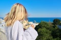 Young woman in bathrobe enjoying cup of coffee and sunny landscape of sea resort, back view Royalty Free Stock Photo